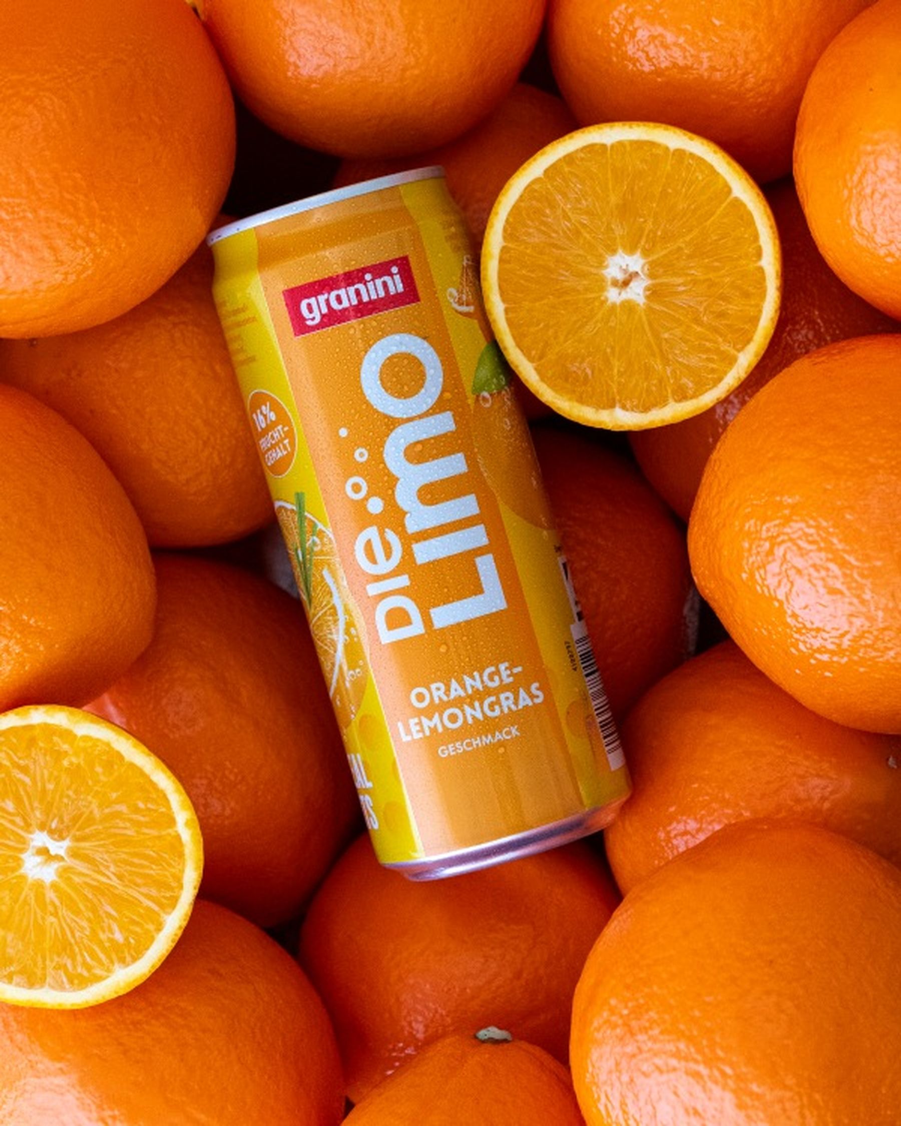A can of "Die Limo" orange-lemongrass drink surrounded by fresh oranges and two halved oranges, showcasing vibrant, juicy textures.