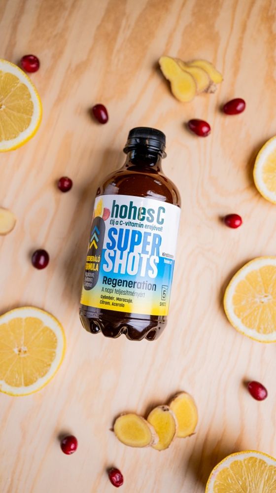 A bottle of hohes C Super Shots placed on a wooden surface, surrounded by lemon slices, cranberries, and ginger pieces.