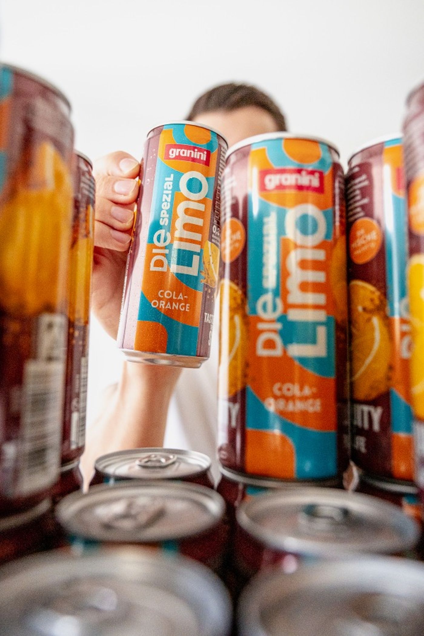 Person holding a can of "Die Limo" cola-orange drink among similar cans, with vibrant blue and orange design.