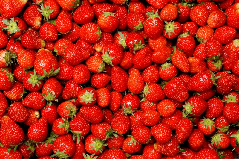 A close-up view of numerous ripe, red strawberries with green leaves, filling the entire frame.