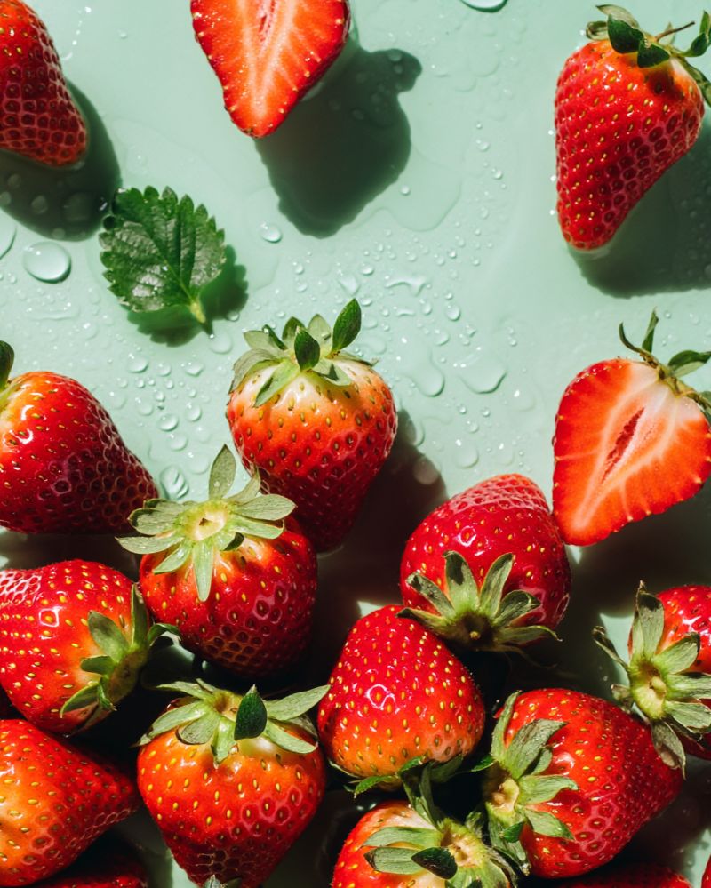 Strawberries Close up Fresh strawberries and a green leaf on a wet, mint-green surface, with droplets scattered around.