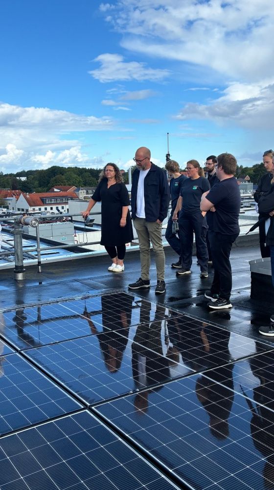 A group of people standing on a rooftop next to solar panels under a blue sky with scattered clouds.