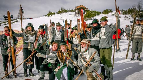 Participants in the nostalgia ski race in traditional costume and ski clothing with start numbers and wooden skis pose in the snow.