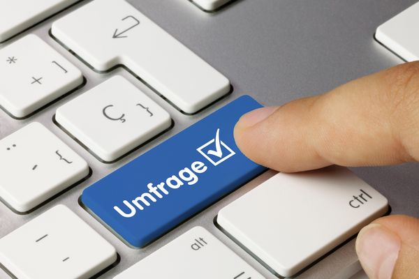 Person, die ein Smartphone mit einer Fünf-Sterne-Bewertungs-Sprechblase darüber benutzt, neben einem offenen Laptop auf einem weißen Schreibtisch.