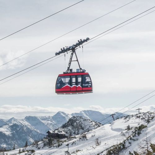 Eine rote Bergbahn gleitet über die verschneite Feuerkogel-Landschaft, im Hintergrund ragen die Berge majestätisch empor.
