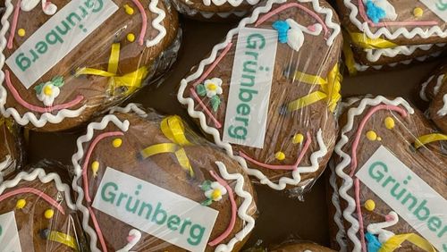 Several decorated gingerbread hearts in bright colors lie on a table, lovingly designed with lettering and sugar decorations.
