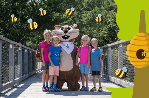 Children and a squirrel mascot stand on a wooden bridge, surrounded by flying cartoon bees and a tree with a beehive.