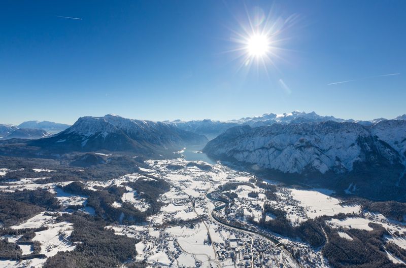 Luftaufnahme einer verschneiten Ortschaft unter blauem Himmel, über der die Sonne hell scheint.