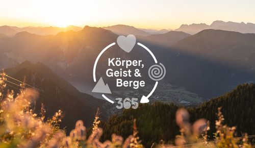 Sonnenaufgang darüber der Text Körper, Geist & Berge 365 mit Herz- und Spiral-Symbolen.