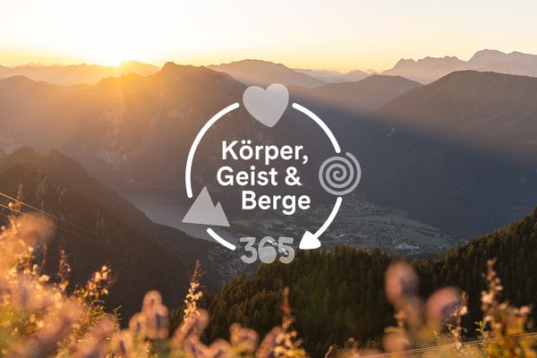 Sonnenaufgang in den Bergen, darüber der Text Körper, Geist & Berge 365 mit Herz- und Spiral-Symbolen.