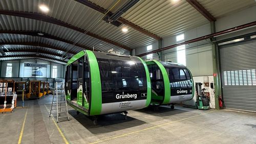 Zwei moderne grün-schwarze Grünberg-Gondelkabinen in einer geräumigen Industriehalle.