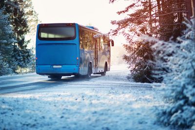 A blue bus drives along a snow-covered road through frosty trees, sunlight streaming through the branches – on the way to the Feuerkogel.