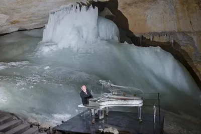 Person spielt transparenten Flügel in einer Eishöhle, umgeben von großen Eisformationen und Felswänden