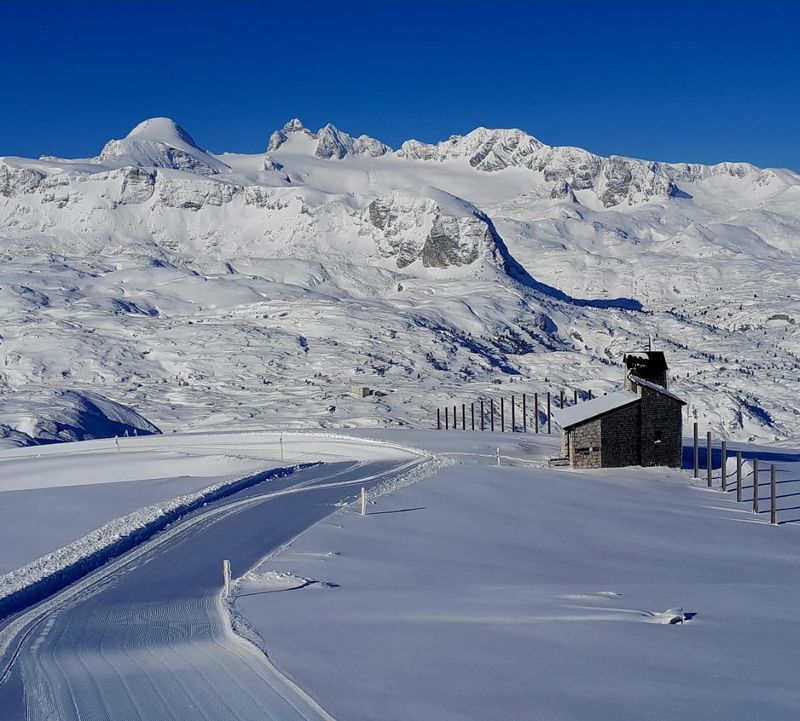 Freshly groomed trail leads to a Heilbronner chapel on the snow-covered Dachstein plateau.