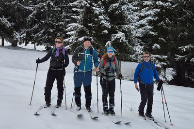 Vier Skitourengeher stehen in einer tief verschneiten Landschaft vor einem Nadelwald.