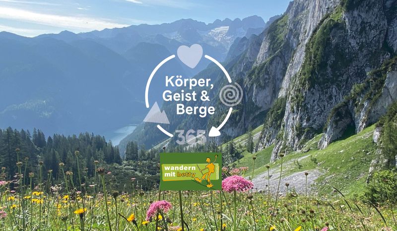 Malerische Berglandschaft mit Wildblumen. Überlagerungen: „Körper, Geist & Berge 365“ und das „wandern mit“-Logo.