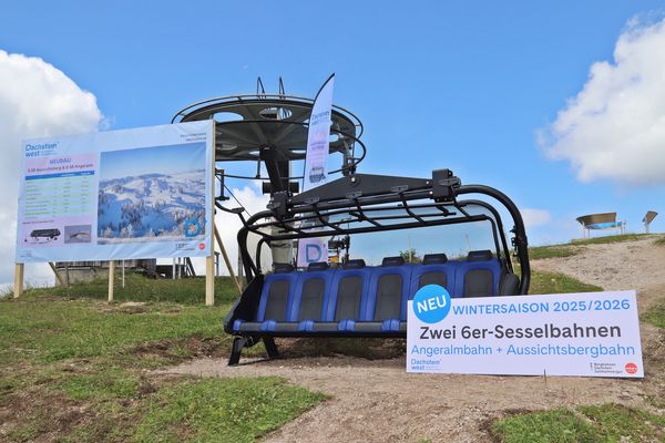 Skiliftsessel auf grasbewachsenem Hügel mit Schildern, die neue 6er-Sessellifte für den Winter 2025/2026 ankündigen; blauer Himmel und Wolken im Hintergrund.