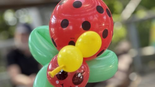 A colorful ladybug made of balloons: red body with black spots, green wings, yellow antennae and a smiling face.