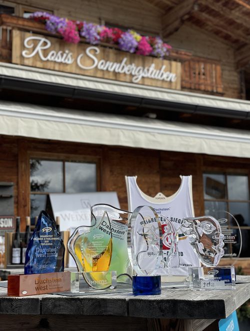 Outdoor table displaying various trophies and a sports jersey, with a rustic building in the background.