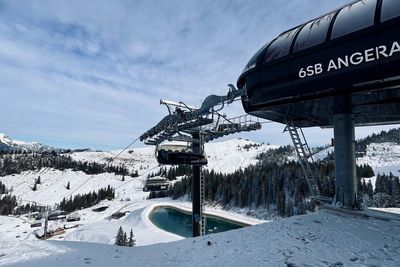 Snowy landscape with a ski lift labeled "6SB Angeralm," trees, and a small snow-covered pond under a cloudy sky.