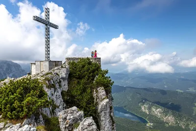 Zwei Frauen stehen am Aussichtspunkt neben dem Europakreuz am Feuerkogel, über ihnen ziehen Wolken durchs weite Panorama.