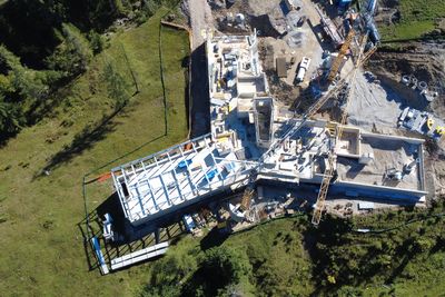 Aerial view of a construction site with partially completed buildings, cranes and surrounding vegetation.