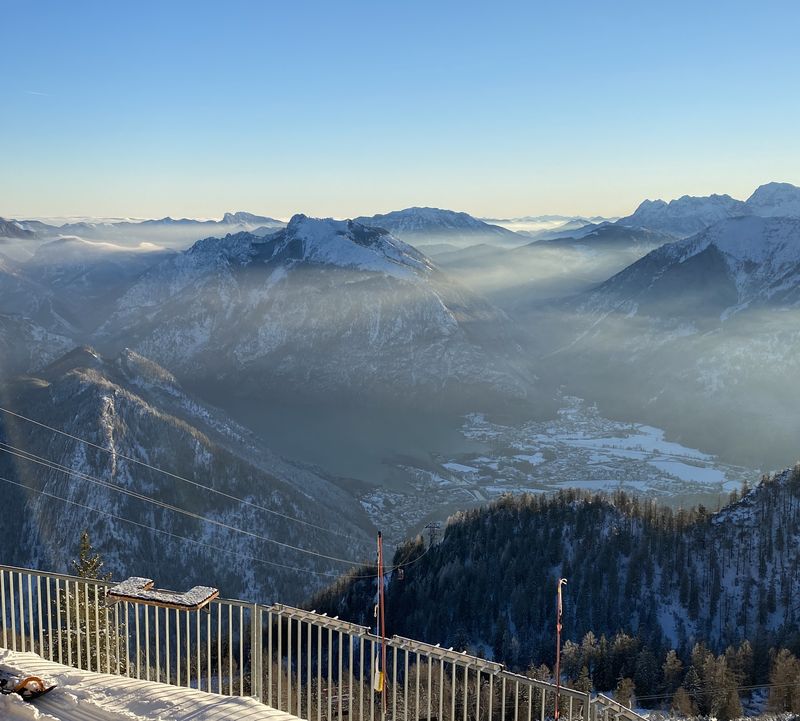 Blick von der Bergstation Feuerkogel auf das verschneite Tal und den Traunsee im goldenen Licht der tiefstehenden Sonne.