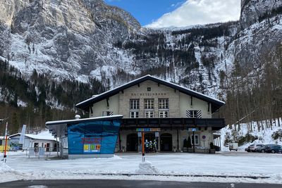 Snow-covered valley station of the Dachstein cable car beneath steep cliffs, people waiting at the entrance.