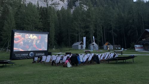 Evening open-air cinema on a meadow, featuring a screen and deckchairs set against a backdrop of wooded mountains.