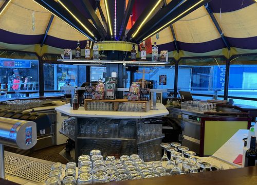 Round bar with colourful canopy, neatly arranged glasses and bottles on display. Large windows look out onto the street.