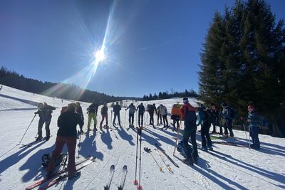 A group of skiers or snowshoers gathers on a sunny, snow-covered slope under a blue sky with bright sunshine.
