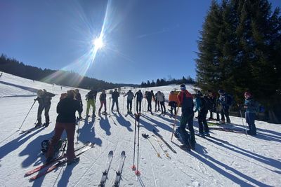 Eine Gruppe Skifahrer oder Schneeschuhwanderer versammelt sich auf einer sonnigen, schneebedeckten Piste unter blauem Himmel mit heller Sonne.