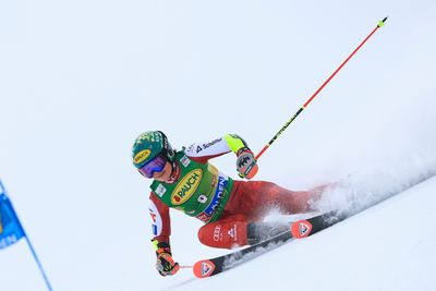 Skirennläuferin im roten Rennanzug fährt in tiefer Kurvenlage über die verschneite Rennpiste und wirbelt dabei Schnee auf.