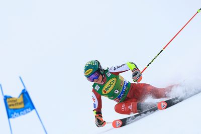Skirennläuferin im roten Rennanzug fährt in tiefer Kurvenlage über die verschneite Rennpiste und wirbelt dabei Schnee auf.