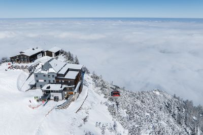 Die Bergstation am Feuerkogel thront auf einem schneebedeckten Grat, darunter schwebt eine rote Gondel durch das Wolkenmeer.