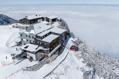 ie Feuerkogel-Bergstation liegt tief verschneit auf einem Plateau über dem Wolkenmeer, eine rote Seilbahn fährt gerade ein