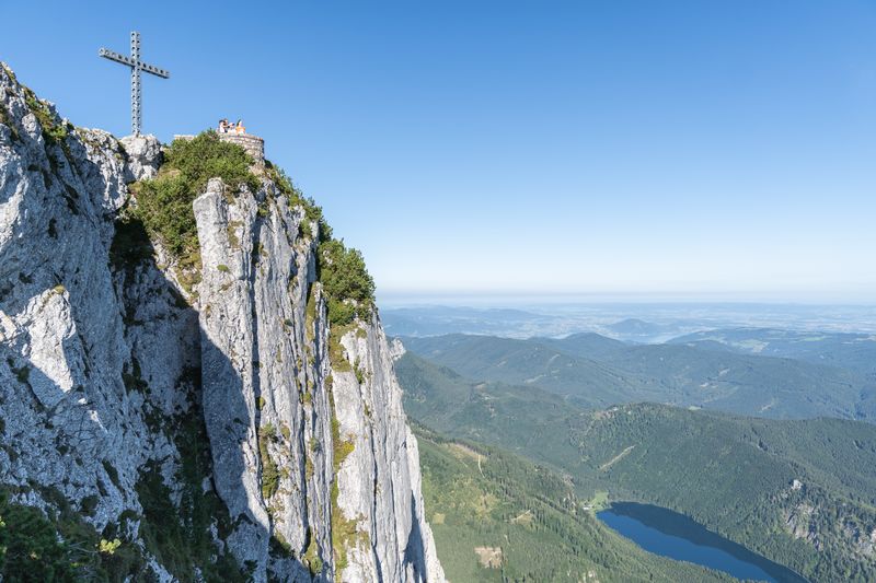 The family stands at the Europe Cross on a steep rocky plateau on the Feuerkogel with a view of the vast Alpine foothills.