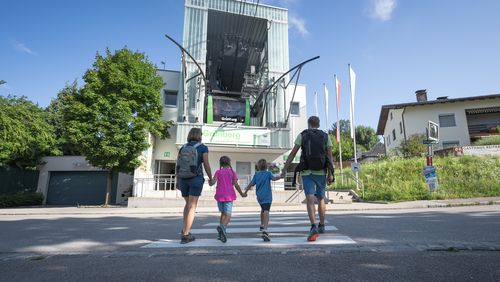 Family with backpacks crosses the road to the Grünberg valley station in the sunshine.