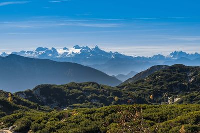 Vor dunklen Hügeln leuchten die schneebedeckten Spitzen des Dachsteinmassivs unter einem klaren, blauen Himmel.