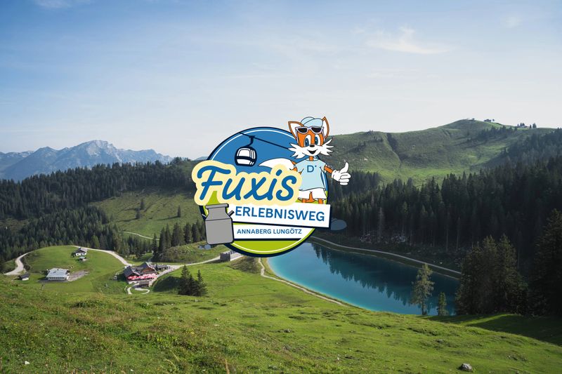 The logo for the ‘Fuxis Adventure Trail’, featuring a cartoon fox, a ski lift and a milk jug, set against a picturesque mountain landscape with a lake and green hills.