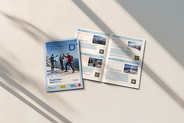 Offene Broschüre mit Wintersportbildern und Text neben einem geschlossenen Umschlag mit Skifahrern in einer verschneiten Landschaft auf hellem Untergrund.