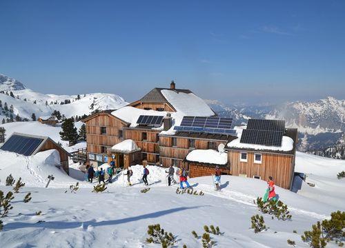 Gruppen von Wanderern erreichen die schneebedeckte Simonyhütte mit Solarpaneelen, umgeben von Winterlandschaft.