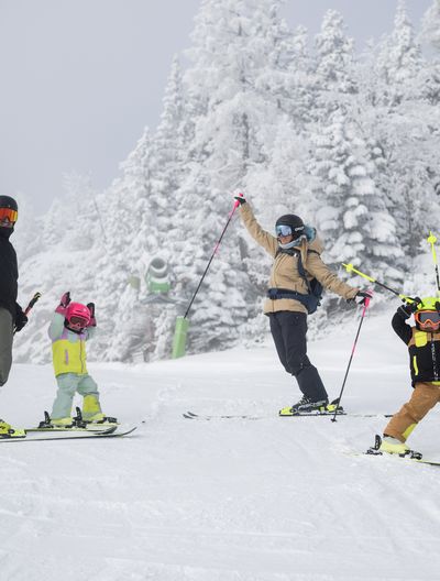 Vierköpfige Familie beim Skifahren auf einer verschneiten Piste am Feuerkogel. Sie posieren fröhlich vor schneebedeckten Bäumen.