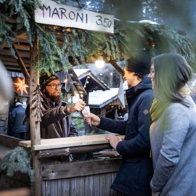 Verkäufer an einem festlichen Maroni-Stand auf einem Wintermarkt überreicht einem Paar eine Tüte.