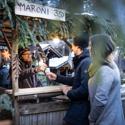 A vendor at a festive roasted chestnut stall at a winter market hands a bag to a couple.