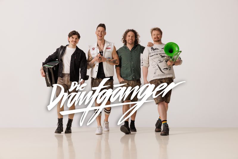 Vier Musiker der Band Die Draufgänger stehen lächelnd mit Instrumenten vor neutralem Hintergrund, der Bandname ist im Bild sichtbar.
