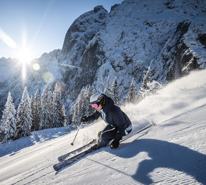 Skifahrerin fährt die Piste in Dachstein West hinunter mit Sonnenstrahlen im Hintergrund