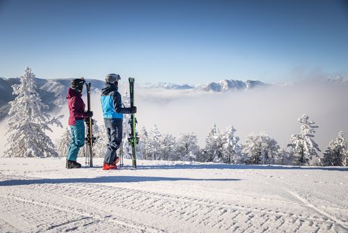Zwei Schifahrer stehen mit Skiern in der Hand auf der Piste in Dachstein West und genießen die Aussicht.