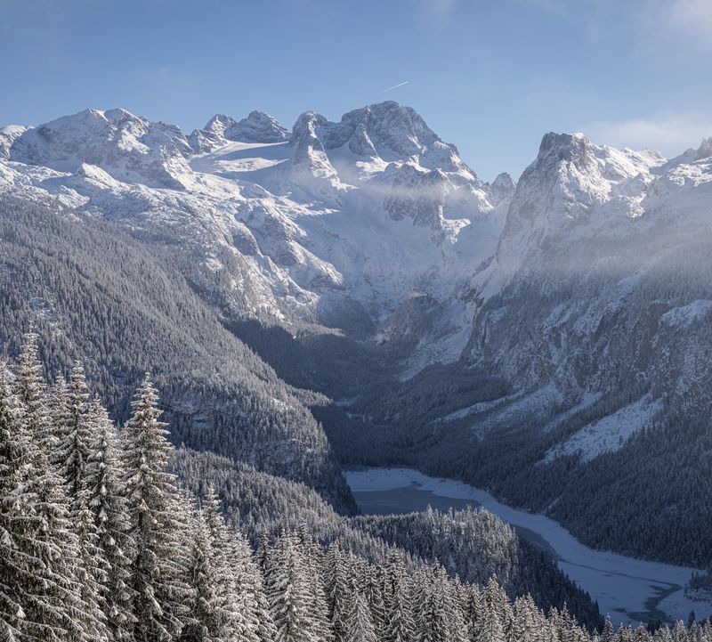 Winter view of the snow-covered Dachstein  with surrounding peaks, snow-covered forests and a frozen lake in the valley.
