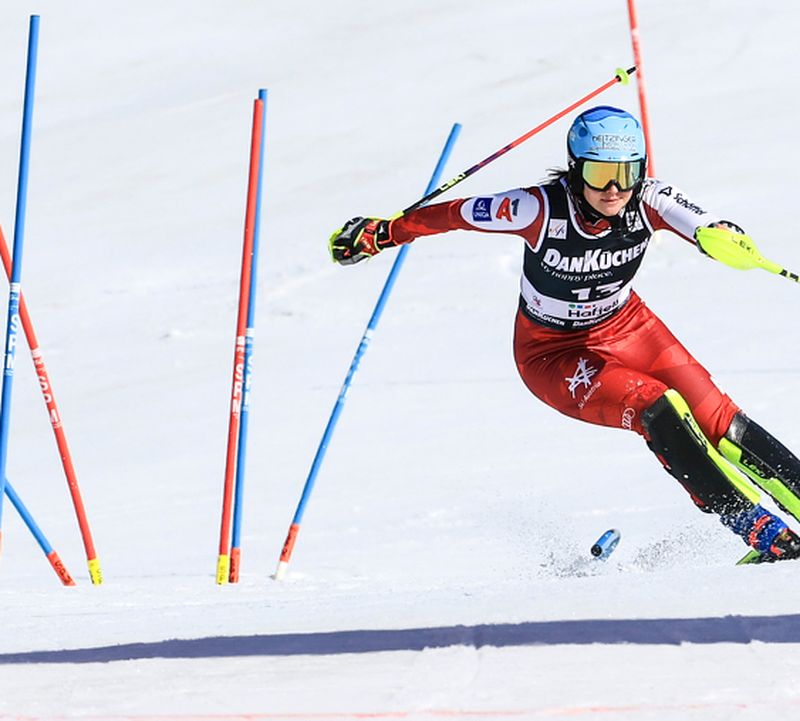 Ski racer in a red suit performing a dynamic slalom run on snow, surrounded by blue and red gates.